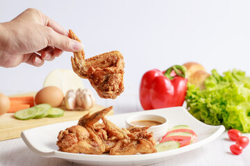 Hand holding fried chicken wings ready for eat on white table.