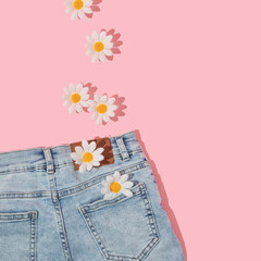 Spring creative layout with faded jeans and white flowers on pastel pink background. 80s or 90s retro romantic aesthetic fashion idea. Minimal romantic summer flat lay.