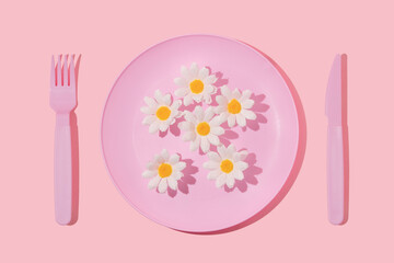 Spring creative layout with pastel pink plate, fork,knife and white flowers on pastel pink background. 80s or 90s aesthetic fashion food restaurant concept. Minimal summer idea.