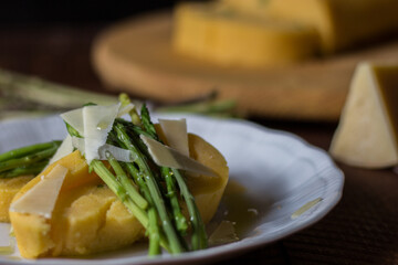 Rolled corn porridge with asparagus and cheese flakes on white plate and dark wood background