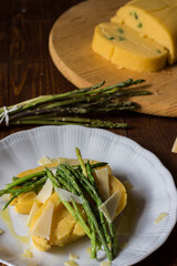 Rolled corn porridge with asparagus and cheese flakes on white plate and dark wood background