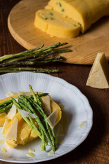 Rolled corn porridge with asparagus and cheese flakes on white plate and dark wood background
