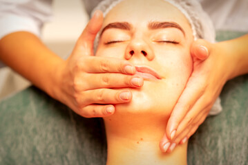 Fototapeta na wymiar Beautiful young caucasian woman with closed eyes receiving a facial massage in a beauty salon