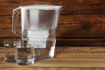 Filter jug and glasses with purified water on wooden table. Space for text