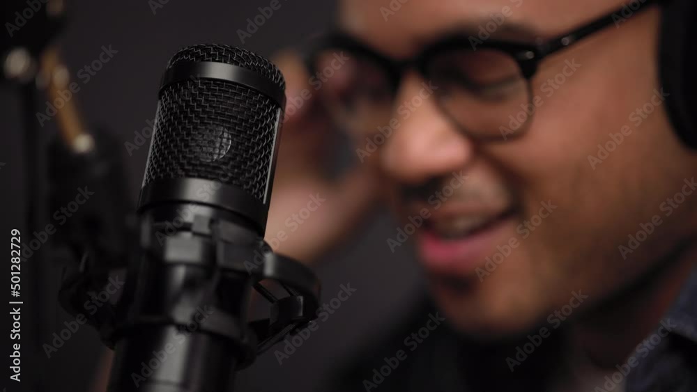 Wall mural Close-up condenser microphone of content creator man host streaming his a podcast on laptop with headphones interview conversation at night broadcast studio. Male blogger recording voice over radio