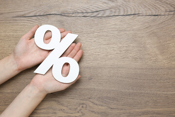 Woman holding paper percent symbol cutout on wooden background, top view. Space for text
