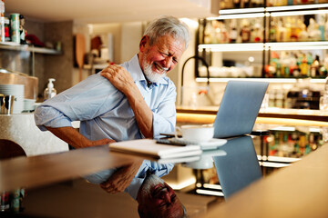 Fototapeta A senior man sits in a coffee shop and has back pain. obraz