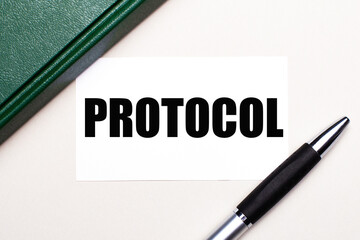 On a light gray background lies a pen, a green notebook and a white card with the text PROTOCOL. Business concept.