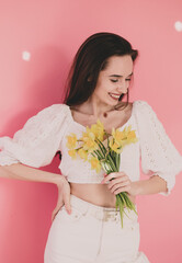 
Woman of model appearance holds yellow flowers in her hands and smiles on a pink background