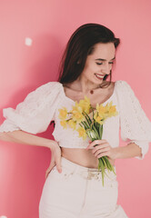 
Woman of model appearance holds yellow flowers in her hands and smiles on a pink background