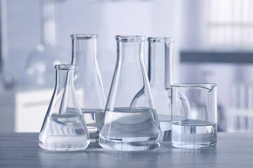 Different laboratory glassware with transparent liquid on wooden table against blurred background