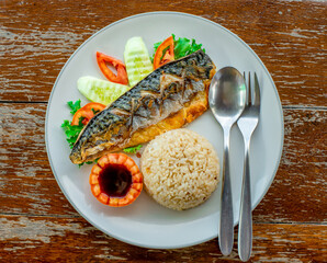 Grilled saba fish served with rice on a plate with dipping sauce.