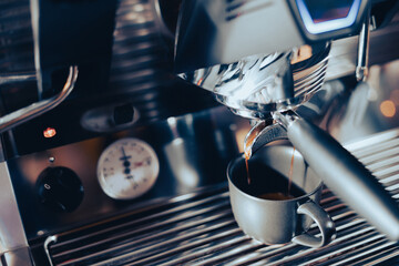 Close-up image of the coffee machine in a coffee shop or restaurant. Barista making coffee extraction from a professional modern espresso brewing machine by a bottomless filter. Cafe Service Concept