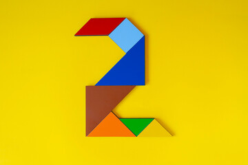 Colorful number 2 made with tangram toy, colored tangram number two isolated on yellow background, kids game idea, teaching counting for children, puzzle toy, top view of second numeric