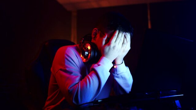 Man is crying and upset after losing an online videogame on laptop, covers face with hands, front view. Young man cries after losing in videogame