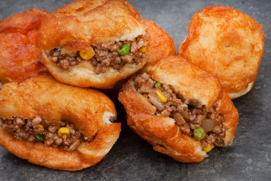 South African vetkoek, deep fried savory dough filled with saucy savory mince on mottled grey background with copy space

