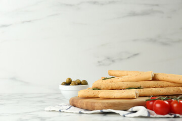 Tasty grissini with rosemary, tomatoes and olives on white marble table, space for text