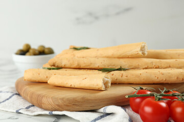 Tasty grissini with rosemary and tomatoes on white marble table, closeup
