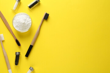 Bowl of tooth powder, brushes and dental flosses on yellow background, flat lay. Space for text
