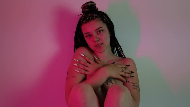 Seductive young woman with braided hair teasing in pink lighting