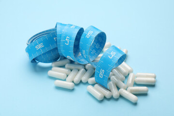 Weight loss pills and measuring tape on light blue background
