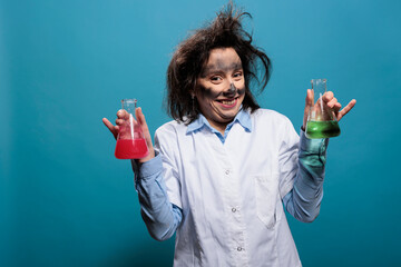 Silly looking mad chemistry expert with messy hair holding glass flasks filled with toxic chemical...