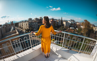 A girl in a yellow dress stands on a balcony during a strong wind