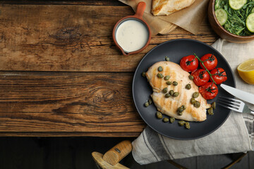Delicious cooked chicken fillet with capers and tomatoes served on wooden table, flat lay. Space for text