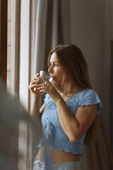 Morning of beautiful young woman drinking water in bedroom next to window.Health care concept photo, lifestyle, close up.