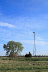A 5G cell phone tower east of Nickerson Kansas USA with blue sky and clouds out in the country with green trees.
