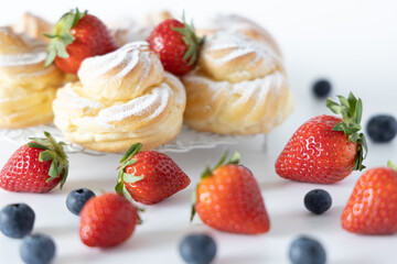 Delicious homemade profiteroles with powdered sugar, strawberries and blueberries. White background.