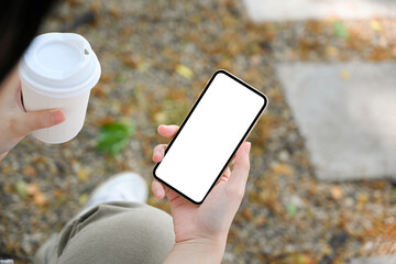 Woman sitting outsides, using smartphone and sipping coffee.