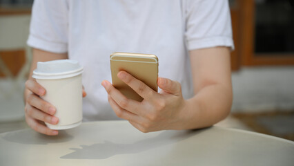 Female relaxes at the coffee shop, sipping coffee and using smartphone.