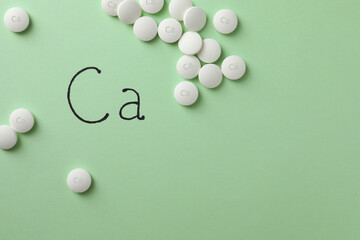 Flat lay composition with calcium supplement pills on light green background, space for text