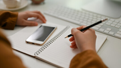 Female student doing her homework at desk, writing on school notebook.