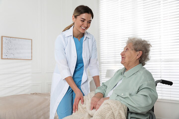 Obraz premium Young caregiver assisting senior woman in wheelchair indoors. Home health care service
