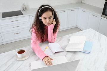 African American woman with modern laptop and headphones studying in kitchen. Distance learning