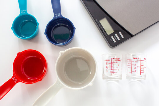 Measuring cups made from colorful plastic and measuring glass with digital scale use in cooking on white background.