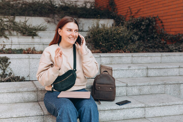 Beautiful smiling female student talking on Phone standing outdoors. Phone Communication. Happy cheerful young woman walking on city street, Urban lifestyle concept. Traveler