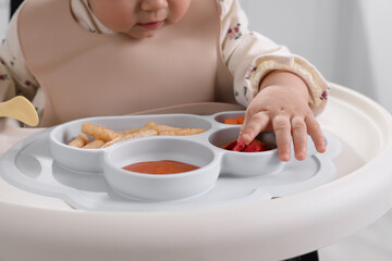 Little baby eating food in high chair indoors, closeup