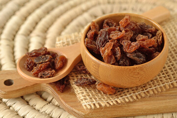 Close-up of raisins in wooden bowl and spoon on wooden chopping board