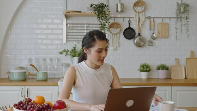 Young Asian Businesswoman Using Computer Laptop Working In Kitchen Room At Home. Work From Home Concept.