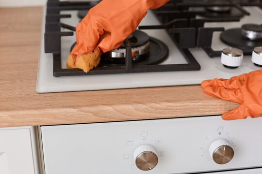 Portrait of girl in orange rubber gloves washes a gas stove, anonymous female doing household chores, cleaning kitchen.