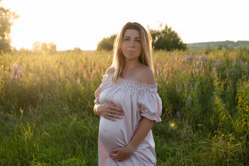 Naklejka na ściany i meble tender pregnancy portrait on sunset. expecting mother to be outside in pink dress. Beautiful tender mood photo of pregnancy.