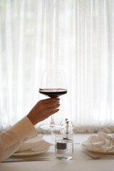 Female hand holding glass of red wine at the window