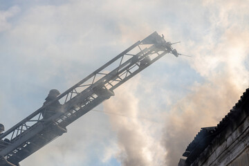 Firefighter works on boom of fire engine. Fireman on sky background. Burning old building in the...