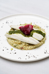 Couscous with fish fillet and beet on a white plate,
