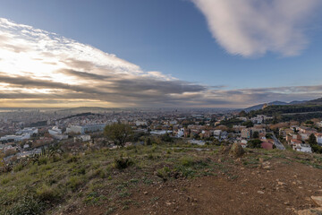 Picturesque landscape of Barcelona from the hill in the early morning. Sunbeams through the clouds. Dramatic sky over the city. Autumn in Barcelona, Spain.