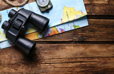 Modern binoculars, map, compass and rope on wooden table, flat lay. Space for text