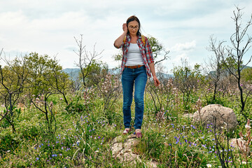 Happy carefree woman walking on a spring meadow with beautiful field flowers. Hiking outdoors, unity with nature.